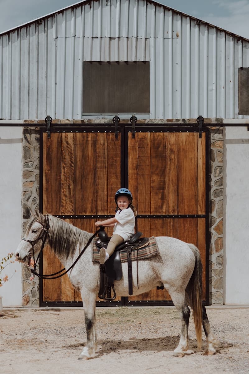 Child riding horse in front of barn
